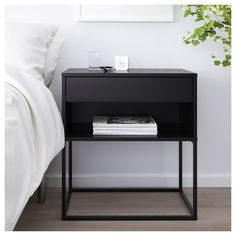 a black nightstand with magazines on it next to a bed