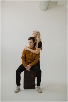 a man sitting on top of a suitcase next to a blonde haired woman with her arms around him