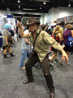 a man dressed up as indiana jones dancing in a convention hall with other people around him