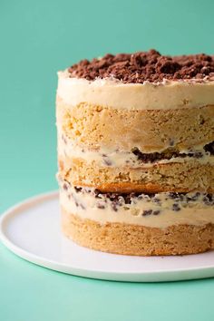 a layered cake with chocolate chips and cream frosting on a white plate against a blue background