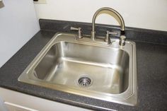 a stainless steel sink in a kitchen with black granite counter tops and white walls behind it