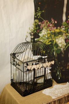 a birdcage sitting on top of a table next to flowers