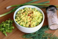 a white bowl filled with food sitting on top of a wooden table next to green onions