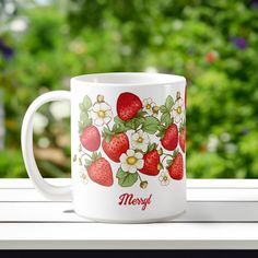 a white coffee mug with strawberries and flowers on it sitting on a window sill