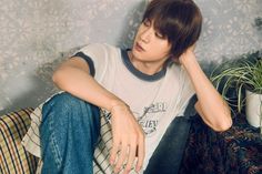 a young man sitting on top of a couch next to a plant