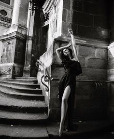 black and white photograph of a woman standing in front of stairs with her arms up