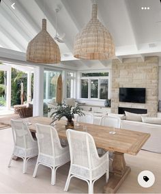 a dining room table with white chairs and wicker lamps hanging from it's ceiling