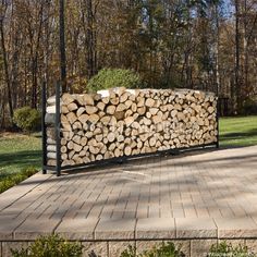 a large pile of logs sitting on top of a brick walkway in front of trees