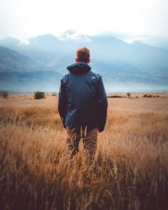 a man standing in the middle of a field with mountains in the backgroud