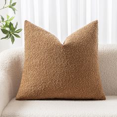 a brown pillow sitting on top of a white couch next to a potted plant