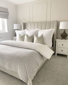 a bed with white linens and pillows in a large room next to a window