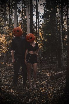 two people with pumpkin heads standing in the middle of a forest at night, one is wearing an orange headband