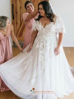 two bridesmaids helping the bride put on her wedding dress in front of them