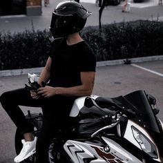 a man sitting on top of a motorcycle wearing a helmet and holding something in his hand