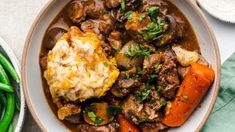 a bowl filled with meat and vegetables on top of a table next to green beans