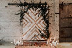 candles and greenery are arranged in front of a wooden paneled wall with an abstract design