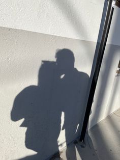 a shadow of a man holding a cell phone up to his face and standing next to a pole