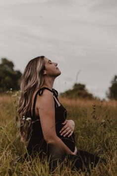 a woman sitting in the grass with her eyes closed and looking up into the sky