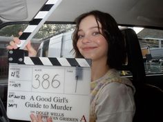 a woman sitting in the back seat of a car holding up a movie clapper