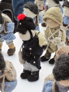 small knitted toy soldiers are lined up on the snow with people in hats and sweaters