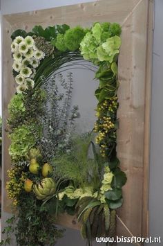 an arrangement of flowers and greenery is displayed in front of a wooden frame on the wall