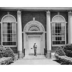 an old black and white photo of a man standing in front of the national bank