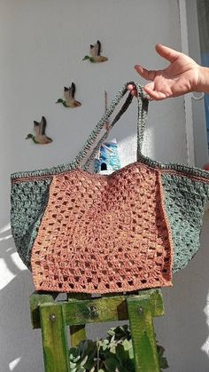 a hand is holding a crocheted bag in front of birds on the wall