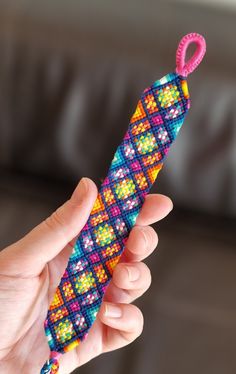 a hand holding a colorful beaded object in it's left hand, with a pink ribbon on the end