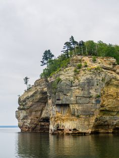 a large rock outcropping in the middle of water with trees on top