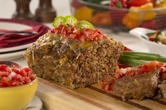 meatloaf with tomatoes and green onions on a cutting board next to a bowl of salsa