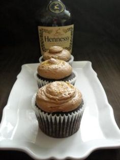 three cupcakes on a plate with a bottle of henness