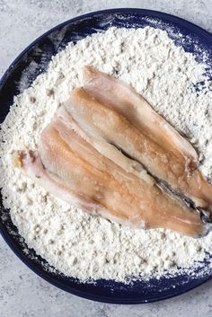 two raw fish fillets in a blue bowl with flour on the side and one partially eaten