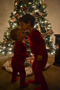 two young children kissing in front of a christmas tree