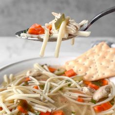 a spoonful of soup with noodles and carrots is being held by a fork