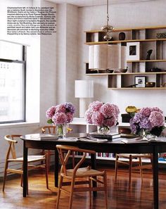 a dining room table with chairs and flowers in vases on the top shelf above it