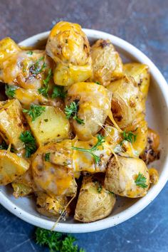 a white bowl filled with potatoes covered in cheese and parsley on top of a blue surface