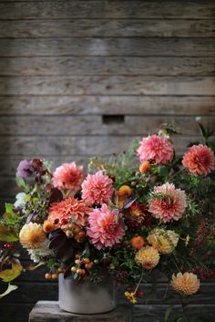 a vase filled with lots of pink flowers on top of a wooden table next to a wall