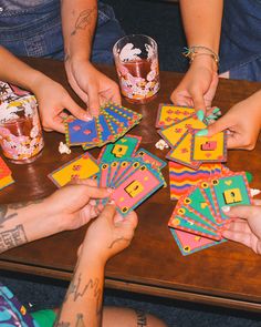 several people sitting around a wooden table playing with matching cards and drinking glasses on it