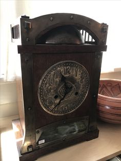 an old clock sitting on top of a wooden table next to a bowl and window