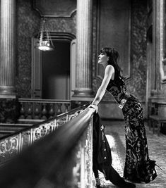 a woman leaning on a railing in an ornate building with columns and pillars, looking up at the sky