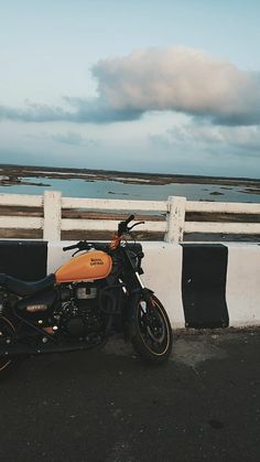 a motorcycle parked on the side of a road next to a white fence and water