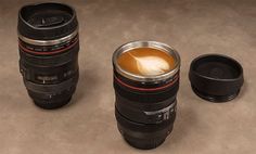 two camera lens cups sitting next to each other on the ground with coffee in them