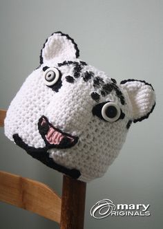 a crocheted animal hat with eyes and ears on a wooden chair against a gray wall