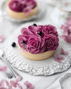 a cupcake with pink icing and purple flowers on it sitting on a doily