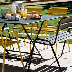 an outdoor table with yellow chairs and breakfast food on it, sitting in the sun