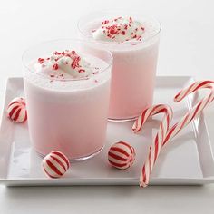 two glasses filled with pink liquid and candy canes on a white plate next to each other