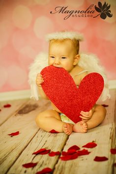 a baby sitting on the floor holding a heart