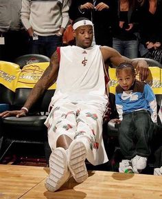 a man sitting on top of a basketball court next to a little boy in front of him