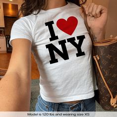 "I Love NY New York" Graphic Slogan Printed On Aesthetic Retro Vintage 90s Y2k Baby Tee Shirt with our own unique font.  🎨 Available in White, Light Pink, Light Blue, Navy, Black. If you need a different color, please let us know! (Ash, Red, Sport Grey & Green)  🎁 Our baby tees are perfect gift for her or him offering timeless fashion and versatility that anyone will cherish. Baby tees, popular in the '90s, have short sleeves and a slightly cropped body, giving a flattering feminine shape. They originated in the skater/raver scene and were part of the era's child-like fashion trend. 🧵 Features : ‣ 90s baby tee style (for adults) ‣ 100% cotton ‣ Double-needle stitched neckline ‣ Seamless collar ‣ Classic fit ‣ True to size (see size chart) ‣ Y2K vintage streetwear fashion 📏 Sizing : Mod I Love New York Shirt Outfit Aesthetic, I Heart Ny Shirt, I Love New York Shirt, I Heart Ny, Baby Tee Shirt, Unique Font, Baby Tee Shirts, Streetwear Mode, Aesthetic Retro