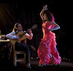 a woman in a pink dress is playing the guitar while a man in a white shirt and tie stands next to her